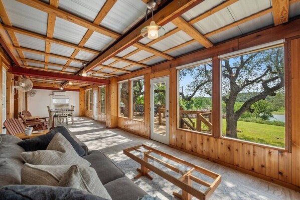 Amplia habitación con techo de madera, ventanas grandes, un sofá y un comedor.