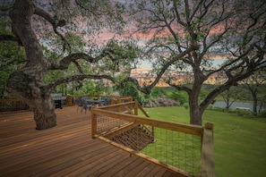 Une terrasse en bois, agrémentée de mobilier d’extérieur, entourée de grands arbres et offrant une vue sur un lac.