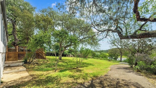 A residential property with a paved driveway, a wooden deck, and a view of a lake. - Lakefront Retreat: Private Dock | King Bedrooms (Burnet County)