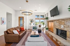 A modern living room with a stone fireplace, leather sofa, and a flat-screen TV. - Tee Box Retreat at Lakecliff Country Club (Travis County)