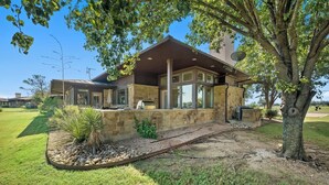 A modern house with a stone exterior, large windows, and a stone patio. - Tee Box Retreat at Lakecliff Country Club (Travis County)
