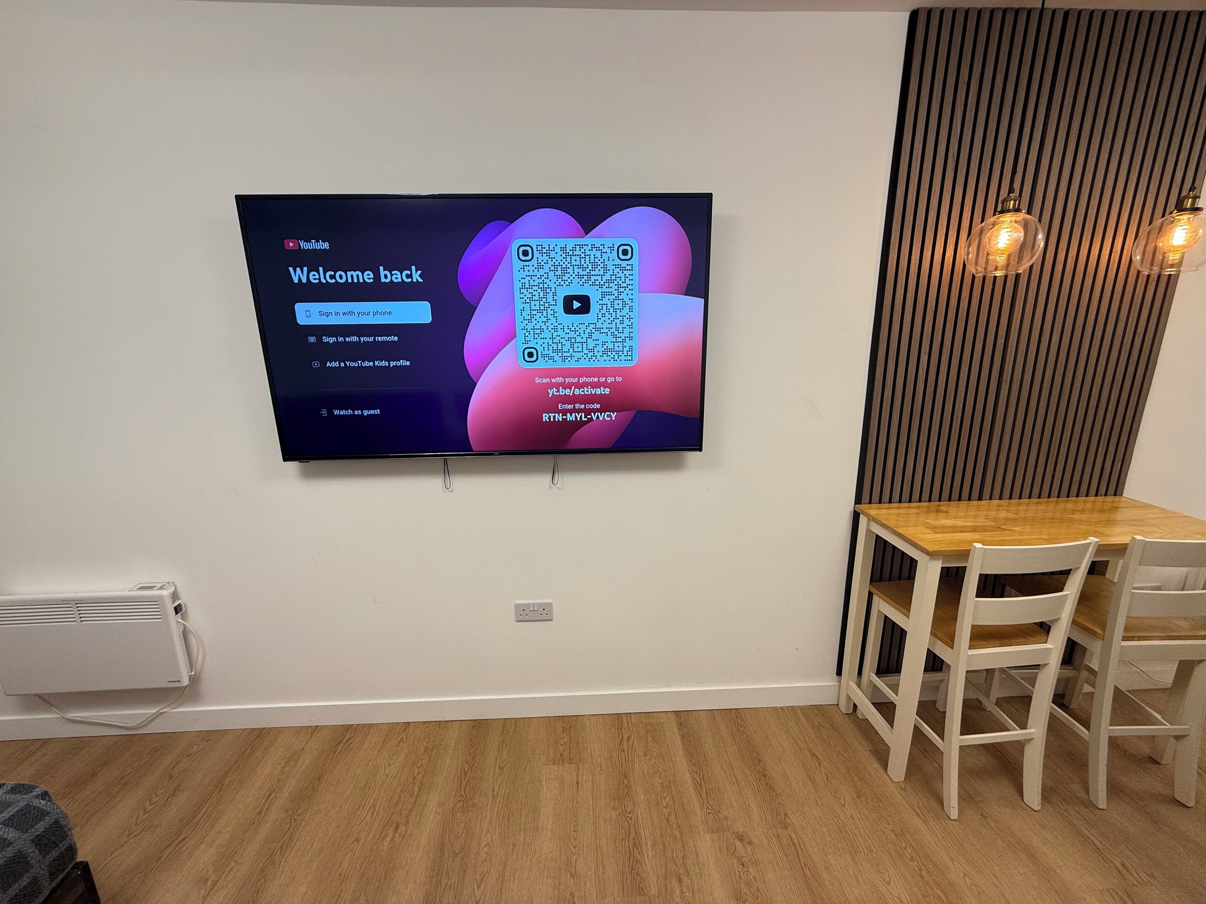 A flat-screen TV mounted on a wall displaying a YouTube Kids sign-in screen.