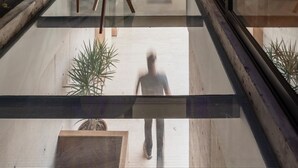 Ein modernes Hotelzimmer mit Glastür, die auf einen Balkon führt, einem runden Holztisch und einem Blumentopf.