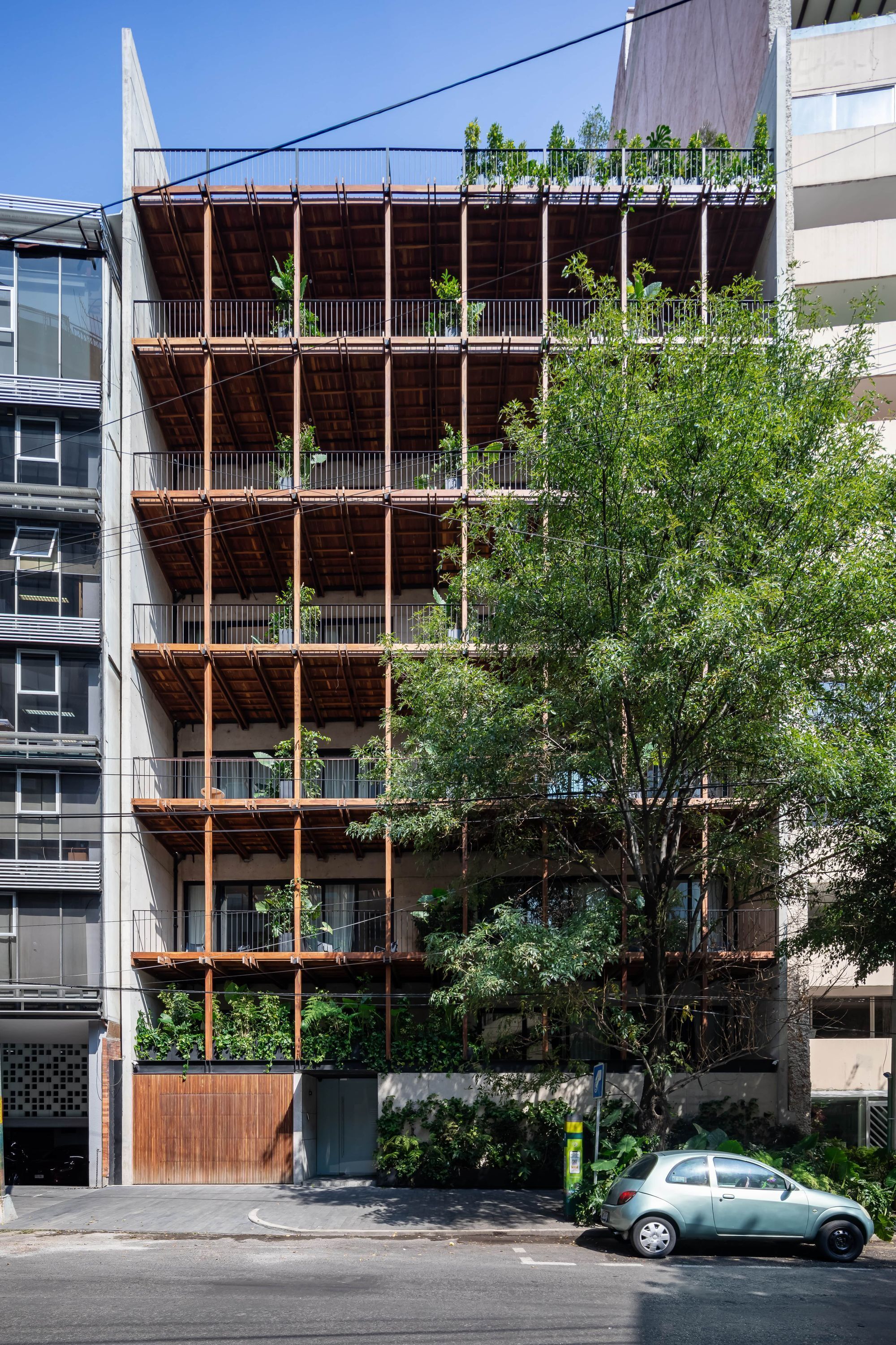 Un immeuble à plusieurs étages, doté d’une façade en bois, de balcons et d’un arbre devant.
