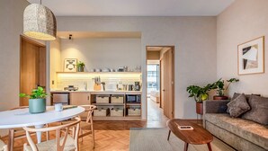 Een moderne woonkamer met een ronde eettafel, houten stoelen, een bank en een salontafel. Achtergrond is een keuken met een magnetron, broodrooster en kastjes.