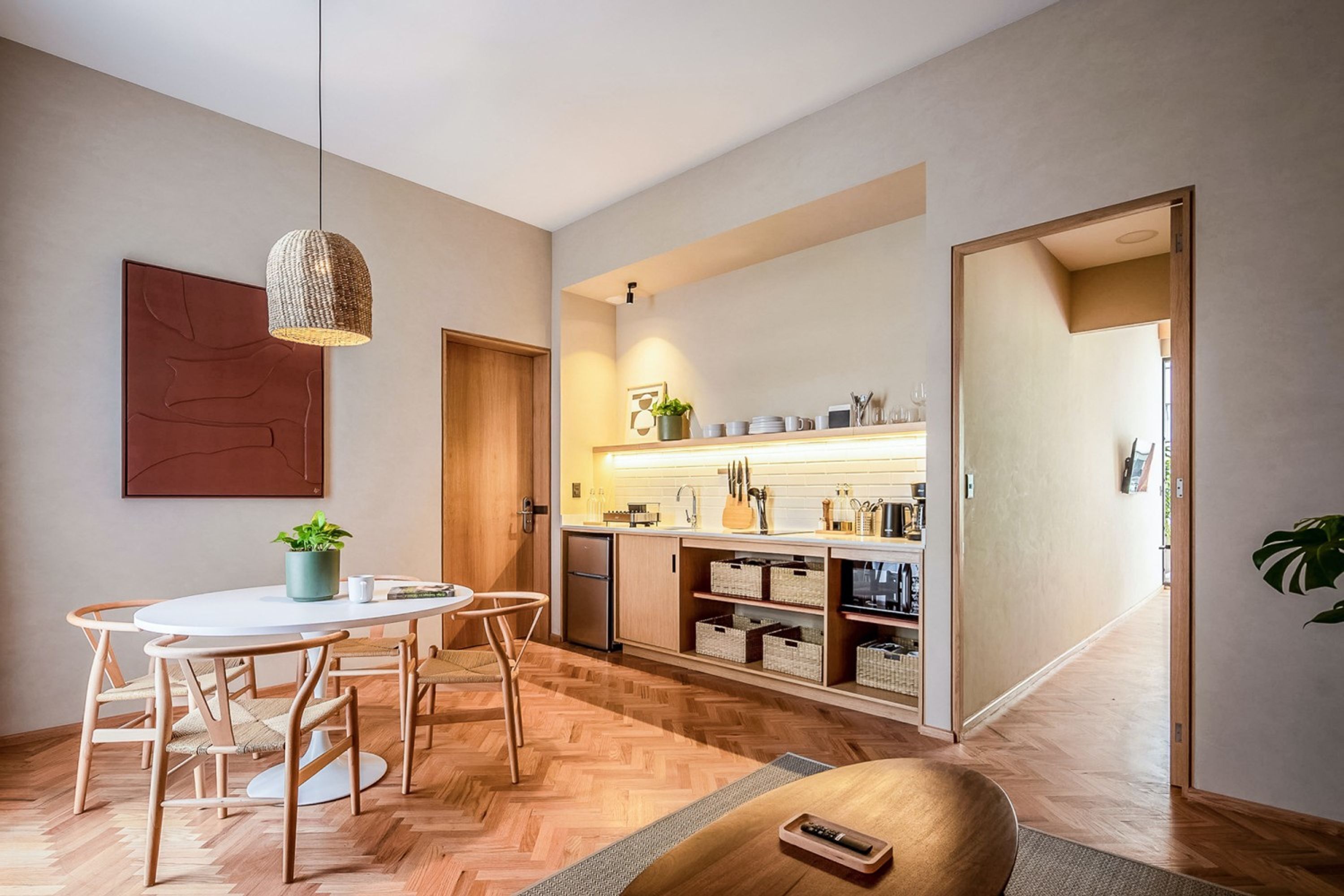 A modern kitchen with wooden cabinets, a dining area with a round table and chairs, and a hanging light fixture.