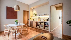 Een moderne keuken met houten kastjes, een eethoek met een ronde tafel en stoelen, en een hanglamp.