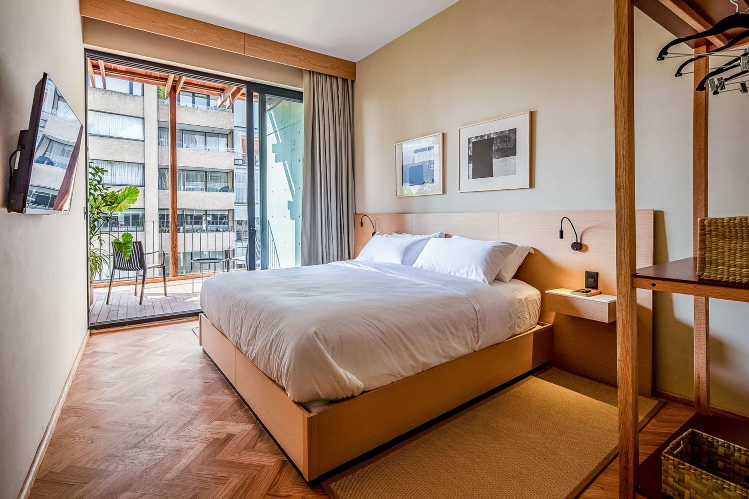 Ein modernes Schlafzimmer mit einem großen Bett, einem Holz-Kopfteil, einem Nachttisch mit Lampe und Blick auf den Balkon.