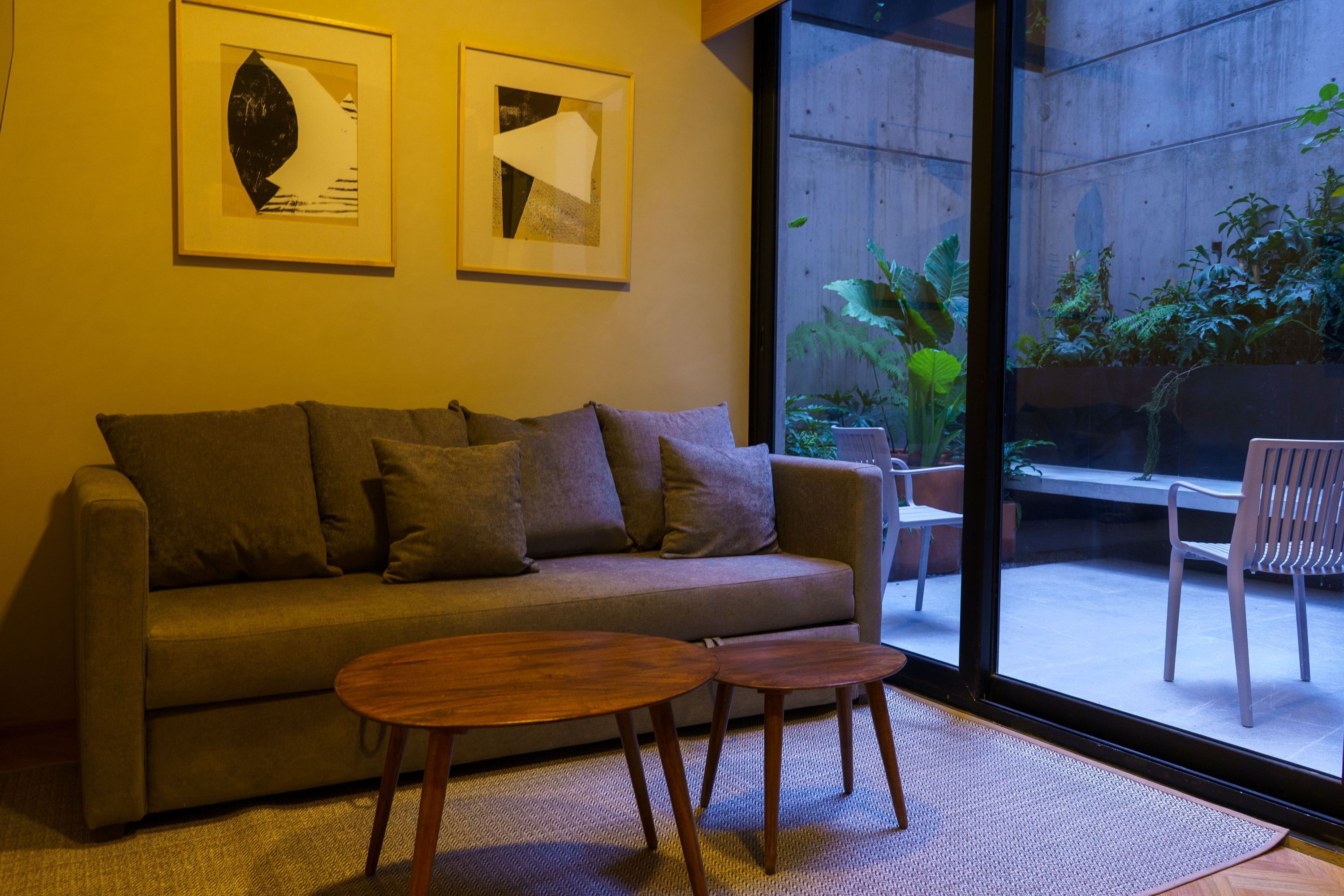 Een moderne woonkamer met een bank, twee bijzettafeltjes en een groot raam met uitzicht op een tuin.