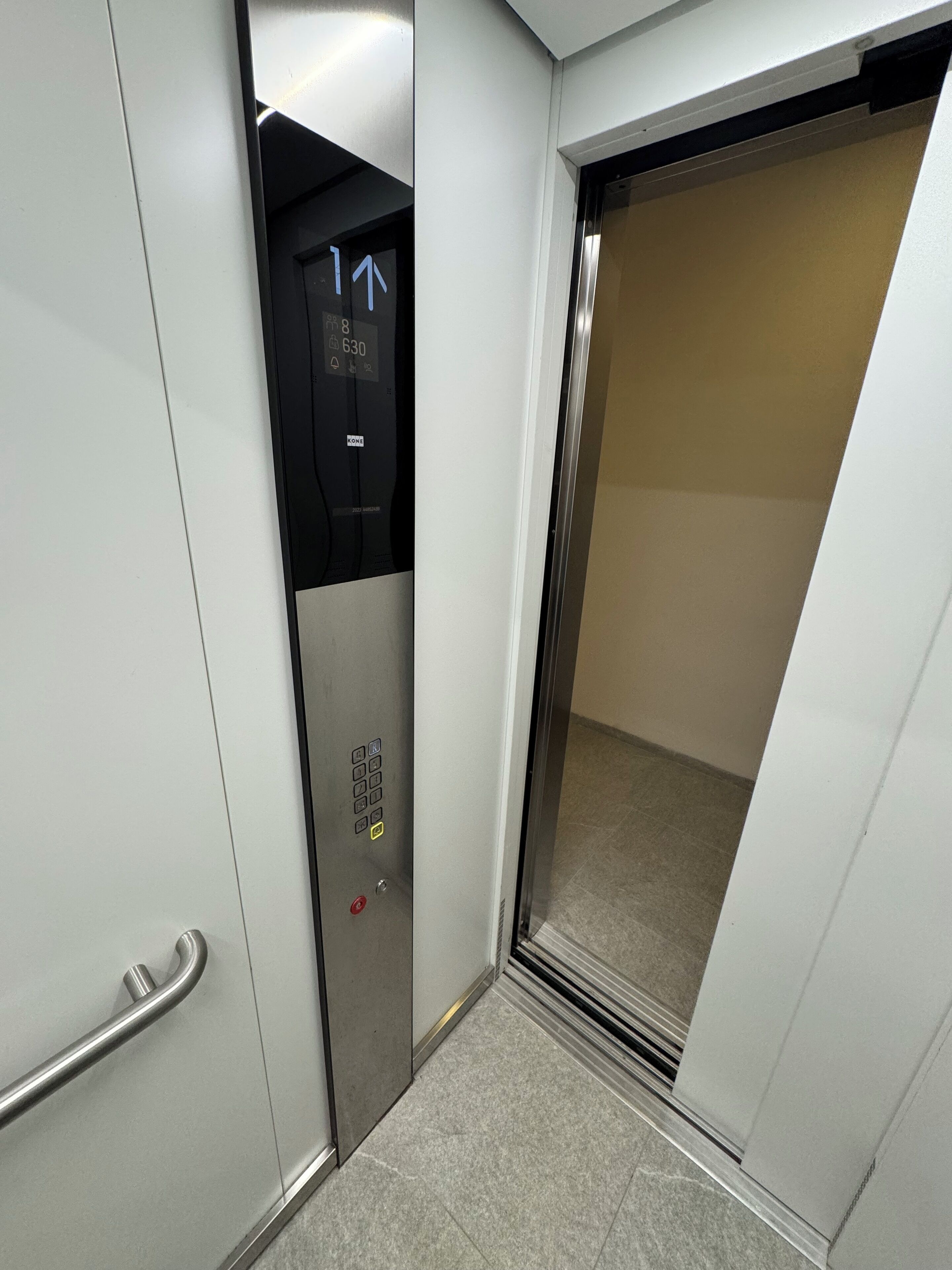 An elevator with a control panel, a red emergency button, and a glass door.