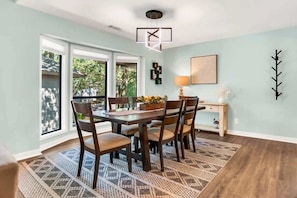 Un espace repas comprenant une table, des chaises, un tapis à motifs, un luminaire suspendu et une vue dégagée grâce à de grandes fenêtres.