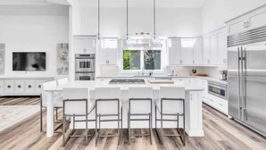 Una cocina moderna con una isla central, armarios blancos, electrodomésticos de acero inoxidable y un amplio ventanal.