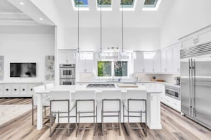A modern kitchen with a central island, white cabinetry, stainless steel appliances, and a large window.