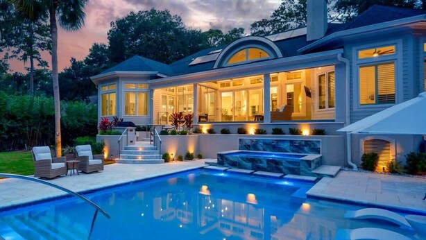 Una casa moderna con piscina, mobiliario de exterior y un patio bien iluminado.