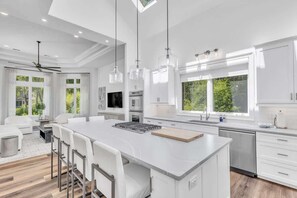 A modern kitchen with white cabinetry, a central island, pendant lighting, and large windows.
