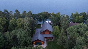 A large house with a garage, surrounded by dense trees and a lake. - Moose Lodge/ Firepit/ Swim/ Pontoon/ Kayaks (Pequot Lakes)