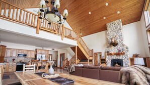A spacious living area with a wooden dining table, a stone fireplace, and a staircase leading to an upper level. - Moose Lodge/ Firepit/ Swim/ Pontoon/ Kayaks (Pequot Lakes)