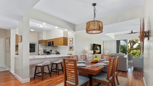 Una cocina moderna con armarios blancos, una isla central y un comedor con sillas de madera y una mesa dispuesta para seis personas.