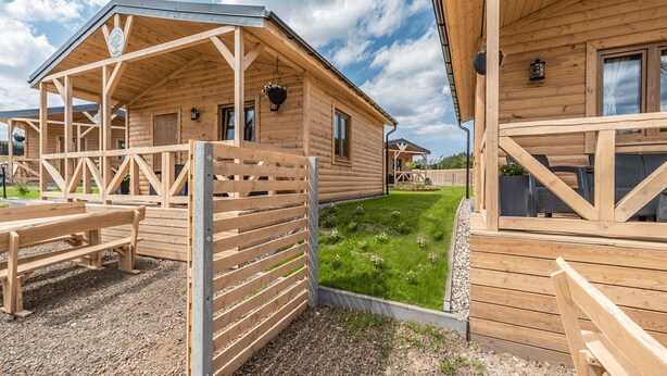 A wooden cabin with a covered porch and a fenced patio area. - Cottage in Duszniki Zdroj With Ski & Spa (Szczytna)