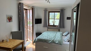 A bedroom with a bed, a desk, and a chair. There is a window with curtains and a view of greenery outside. - Apartment Blueberry Pool Sauna Netflix WIFI (Zwiesel)