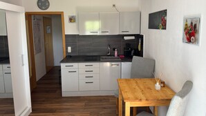 A compact kitchen with white cabinets, a wooden dining table, and a gray chair. - Apartment Blueberry Pool Sauna Netflix WIFI (Zwiesel)
