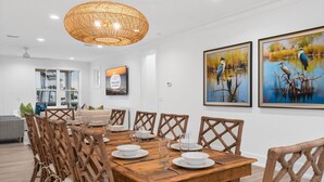 A dining area with a wooden table set for six, surrounded by wicker chairs. There are two framed paintings on the wall depicting birds and water. - Sail Away: Private Pool, Hot Tub, Pet Friendly (Mexico Beach)