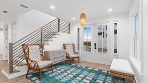 A spacious room with a wooden staircase, wicker chairs, a white bench, and a patterned rug. - Sail Away: Private Pool, Hot Tub, Pet Friendly (Mexico Beach)