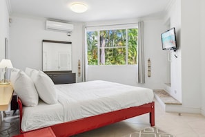A bedroom with a bed, a television, a window with a view of greenery, and a door.