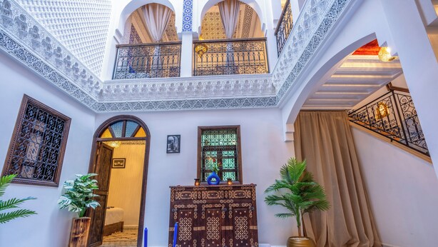Een traditioneel Marokkaans interieur met een binnentuin, gedetailleerd houten meubilair en een betegelde vloer.