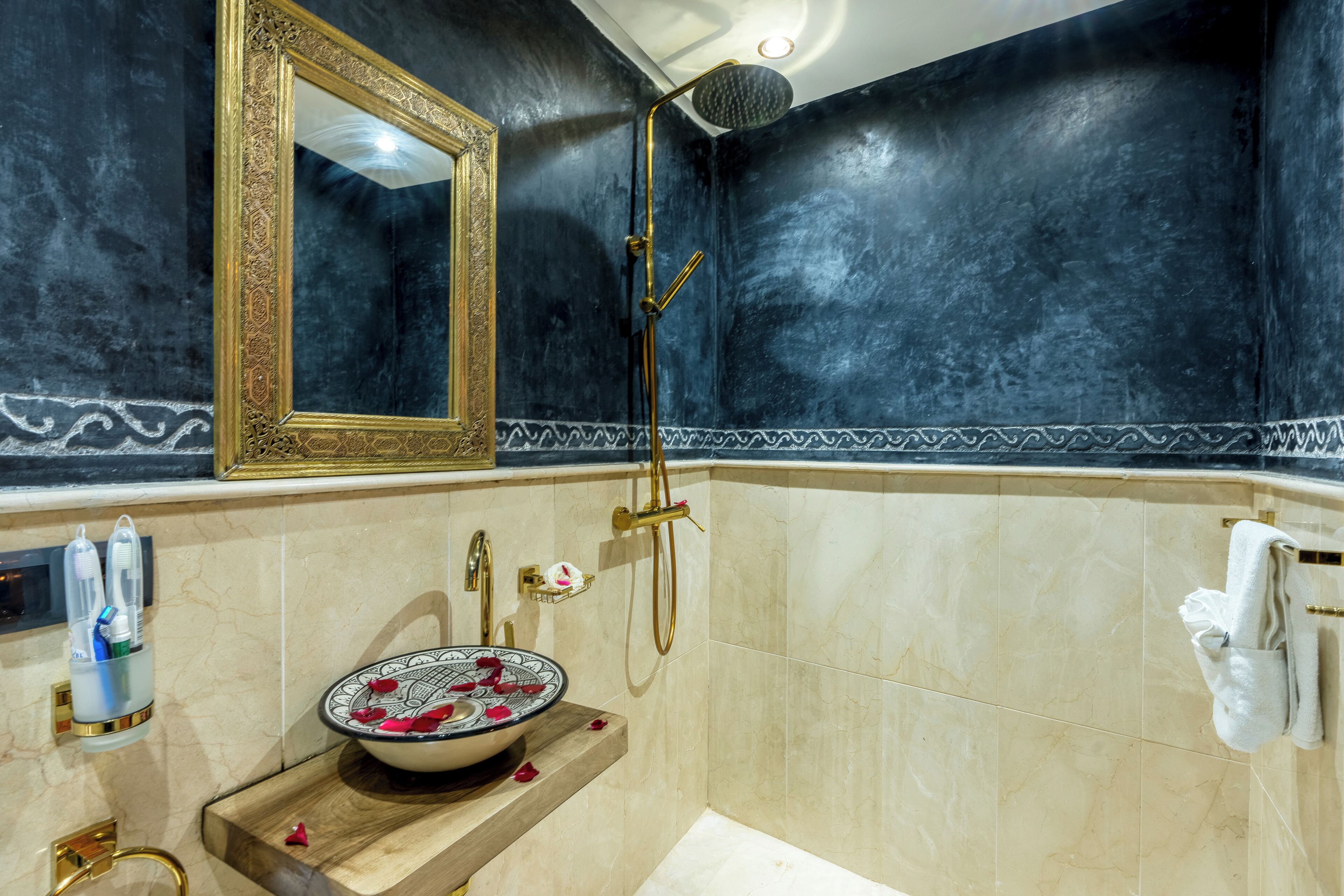 Ein Badezimmer mit Marmorwaschbecken, einem spiegel mit goldener Rahmung, einer Handbrause und einem Handtuchhalter.