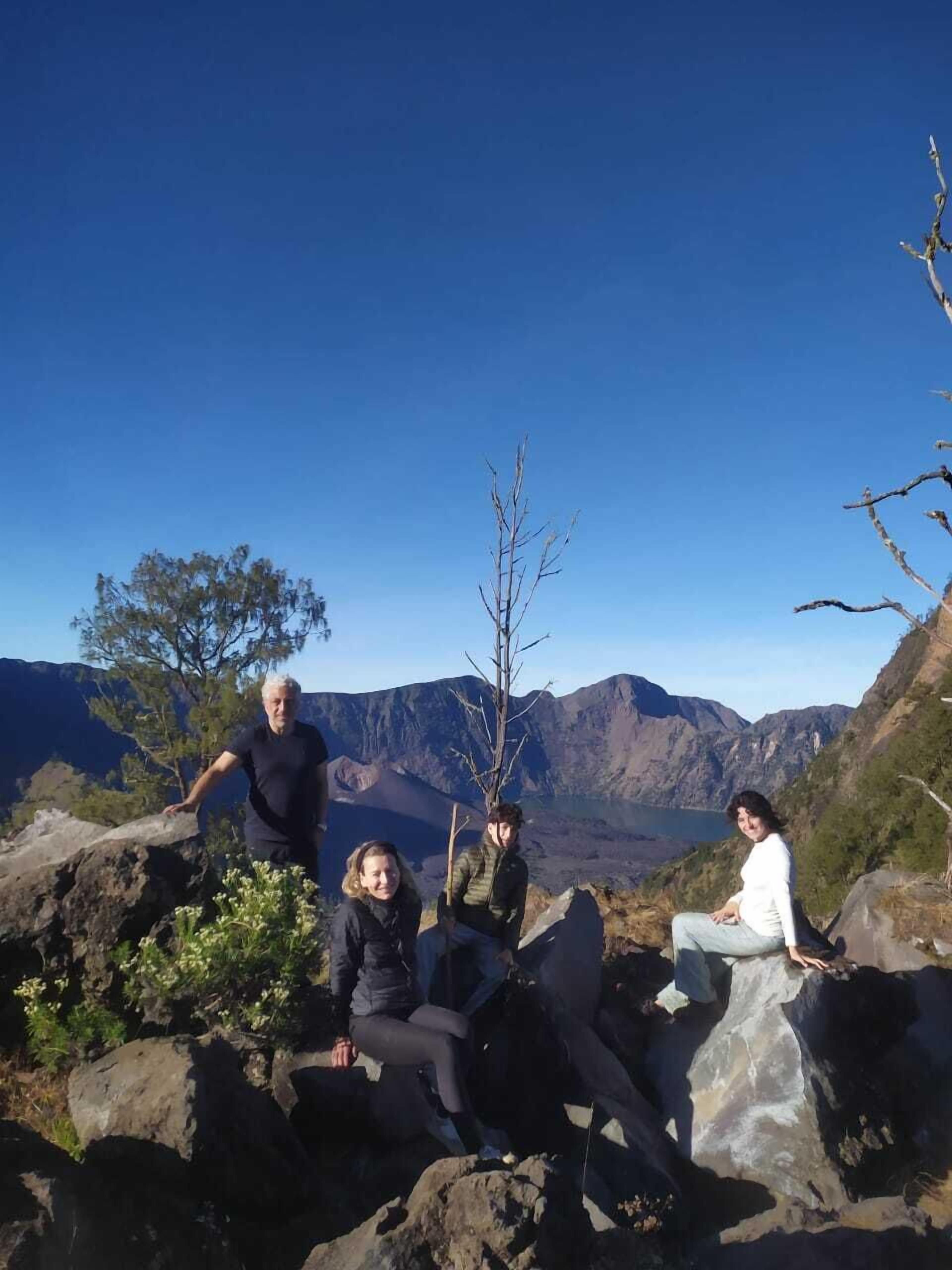 Um grupo de pessoas sentadas em pedras, com uma paisagem montanhosa ao fundo.