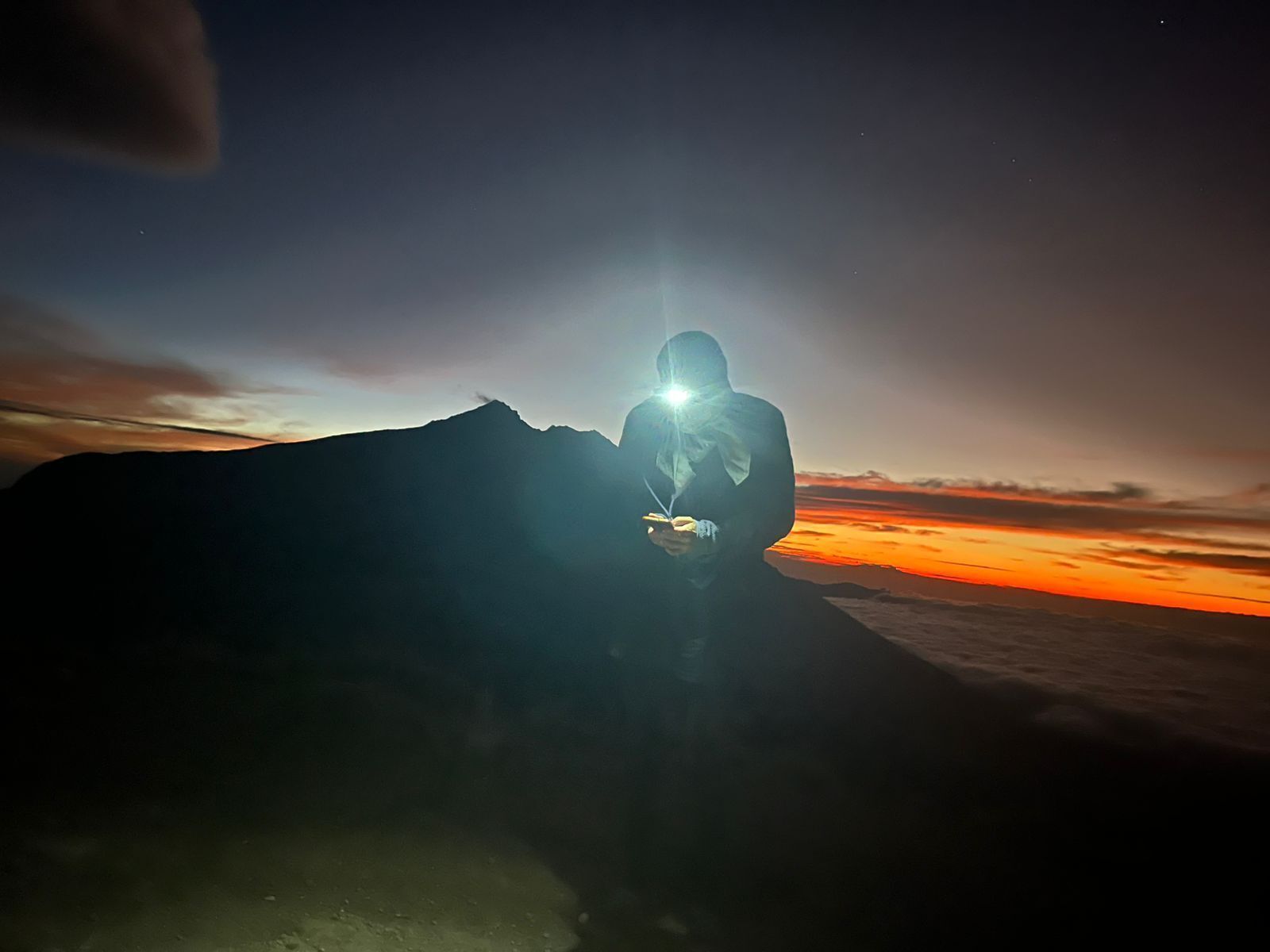 A person sitting on a mountain with a sunset in the background.