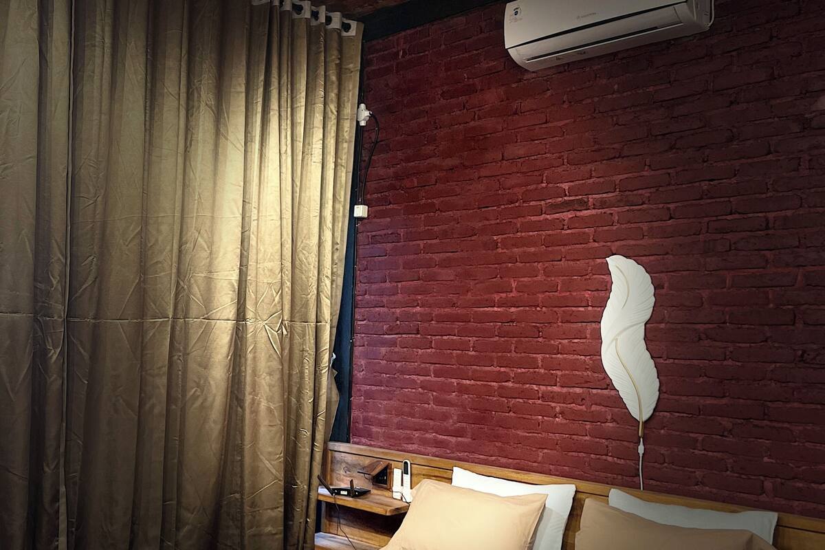 Une chambre avec un lit, des rideaux, un élément de décoration en plumes et un appareil de climatisation.