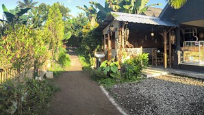 A pathway leading to a rustic building with a thatched roof, surrounded by lush greenery and banana trees. - Tetebatu Valley Bungalows  (Tetebatu)
