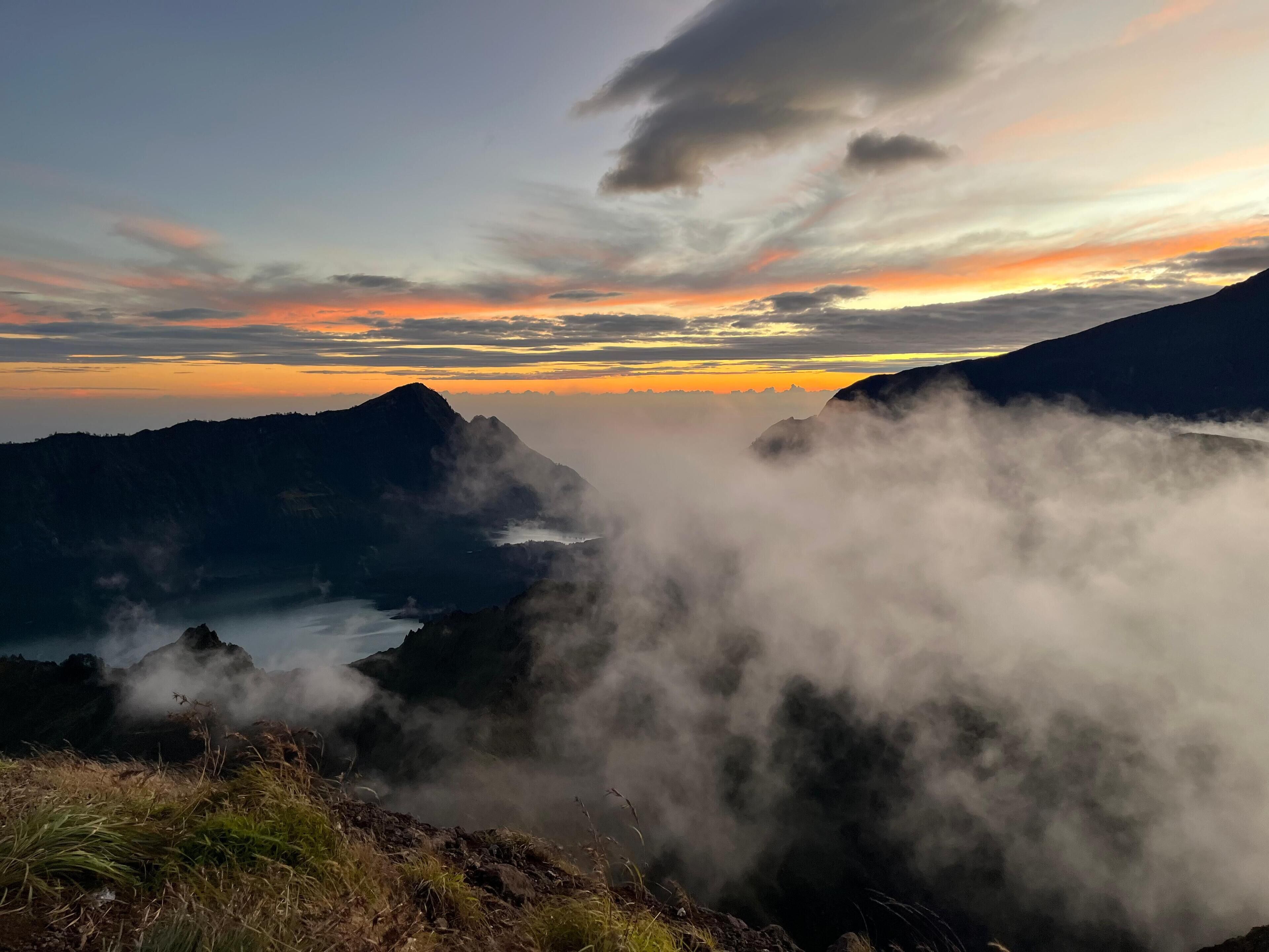Un paisaje montañoso con un valle y un lago, rodeado de nubes y neblina.