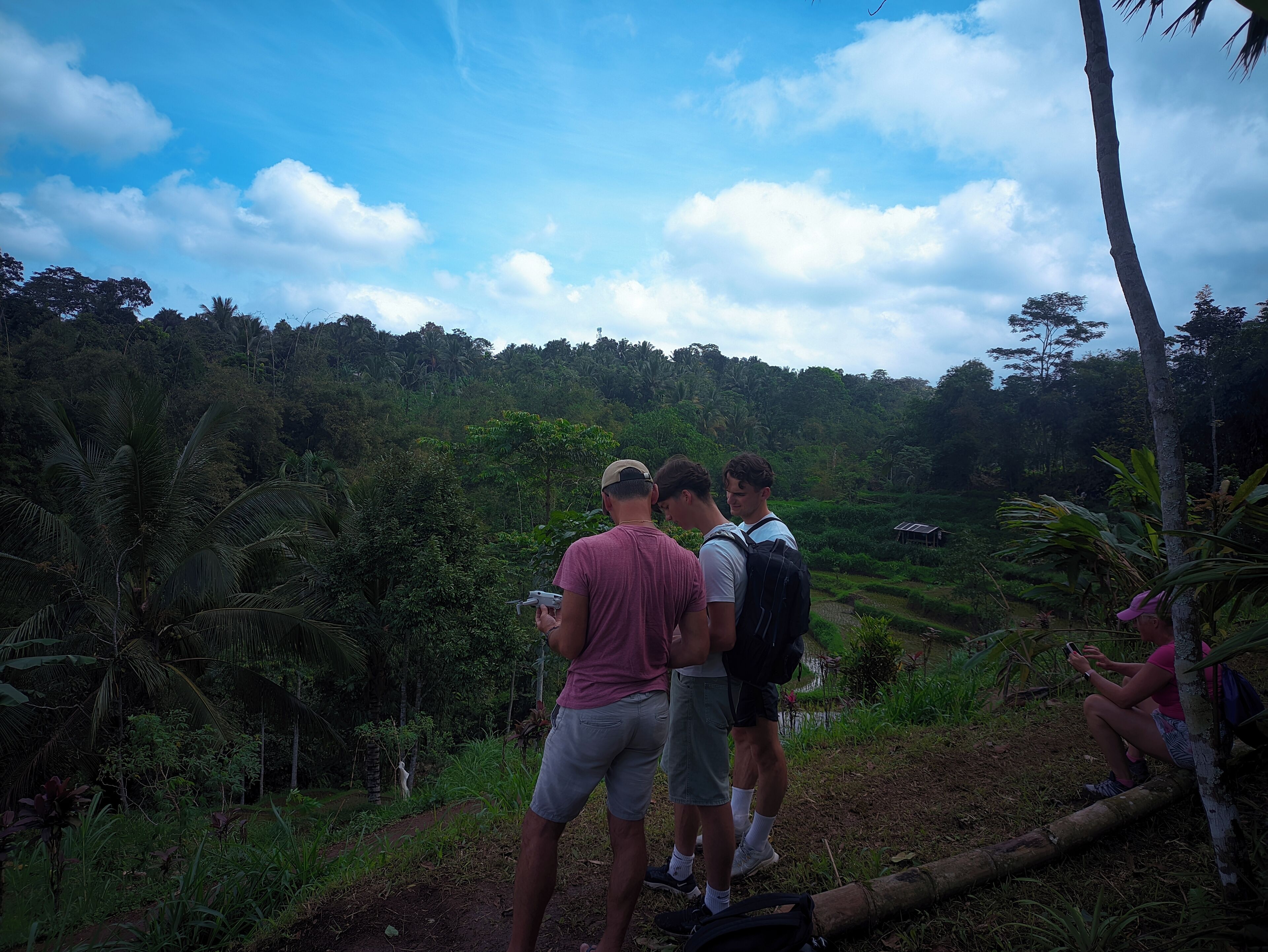 A group of people standing on a dirt path in a lush, green forested area with a clear sky.