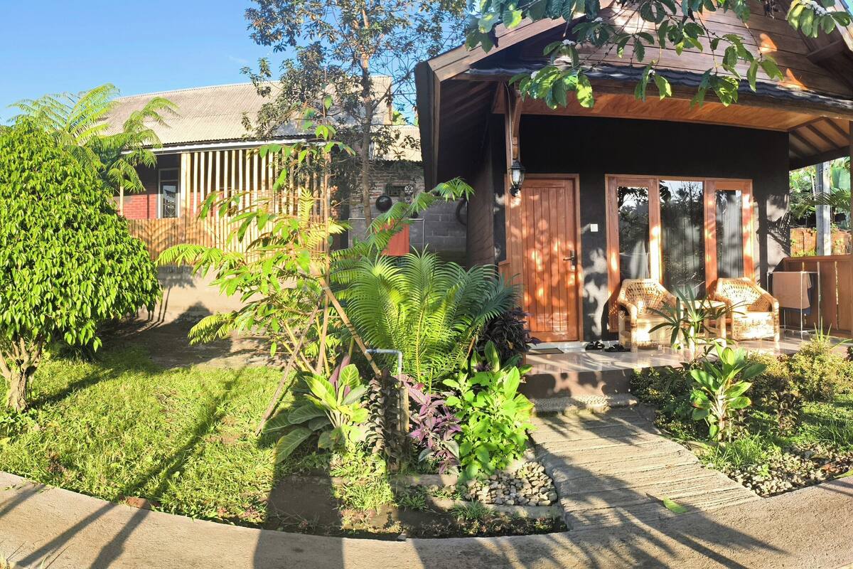 Un jardin avec une terrasse en bois, un mur en briques et un bâtiment doté d’une porte et de fenêtres en bois.
