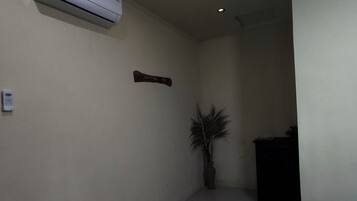 A narrow hallway with a ceiling-mounted air conditioner, a potted plant, and a dark piece of furniture.