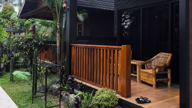 A modern house with a wooden deck, a seating area with a chair, and a garden with various plants. - Tetebatu Valley Bungalows  (Tetebatu)