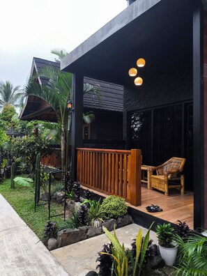 A modern house with a wooden deck, a seating area with a chair, and a garden with various plants. - Tetebatu Valley Bungalows  (Tetebatu)