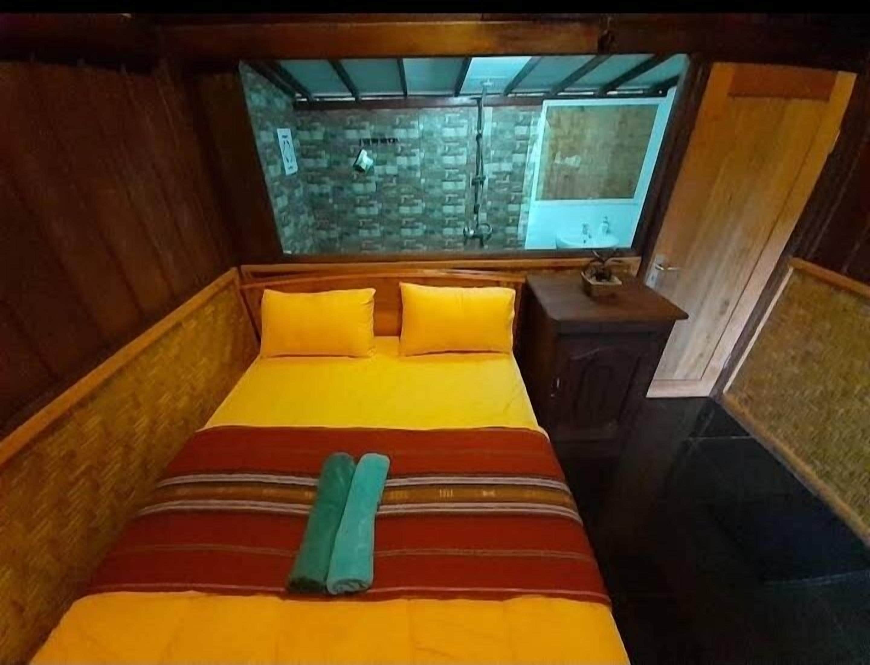 A wooden room with a bed, a small table, and a window.