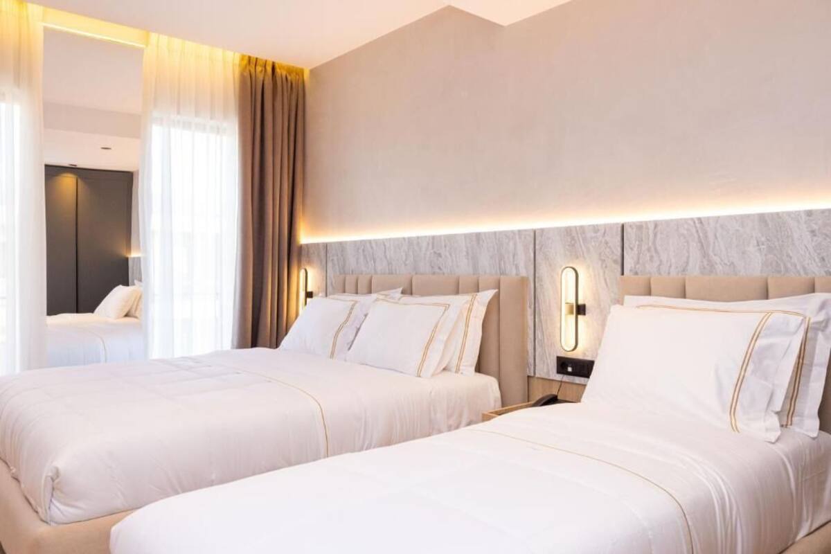 A hotel room with two beds, a marble headboard, a nightstand, and a mirror.