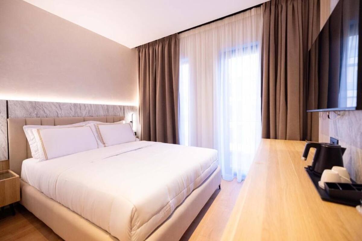 A hotel room with a large bed, a wooden desk, a coffee machine, and a TV mounted on the wall.