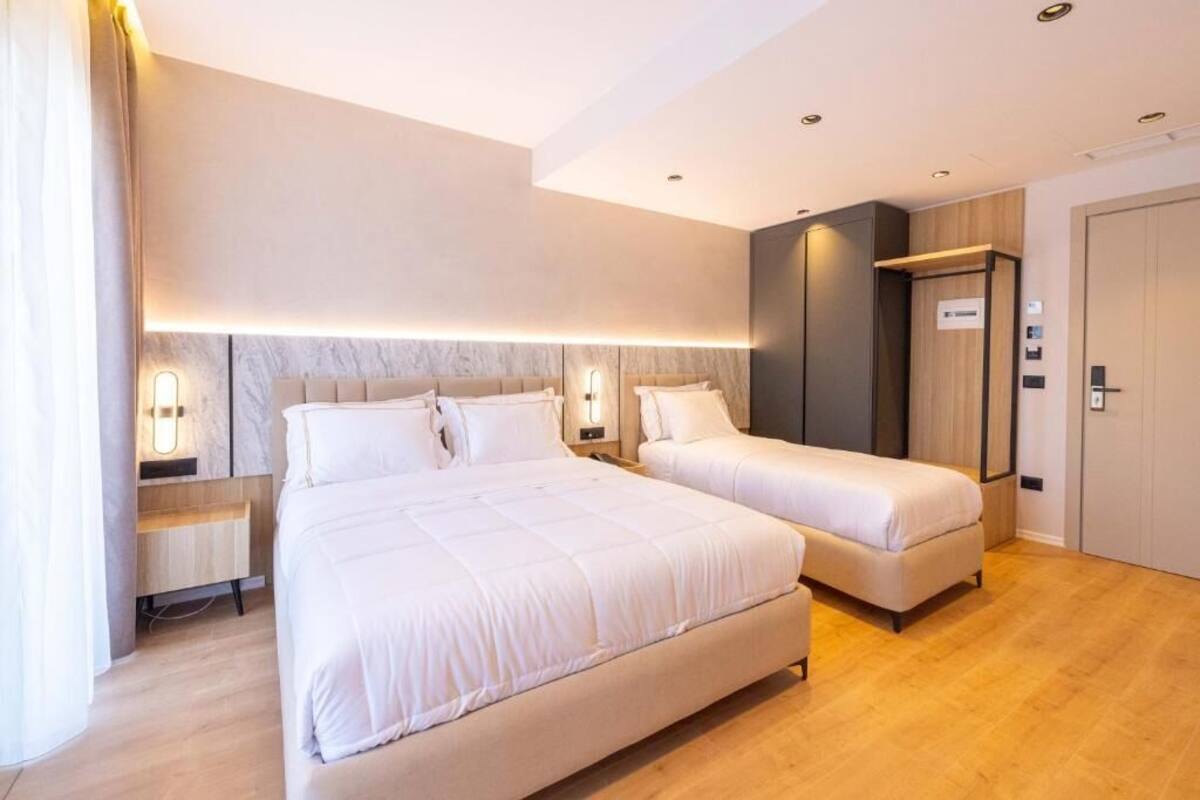 A hotel room with two beds, a wooden floor, a marble headboard, and a modern light fixture.