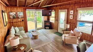 L’intérieur chaleureux d’un chalet avec un plafond en bois, une cheminée, un canapé, une table à manger et un téléviseur.