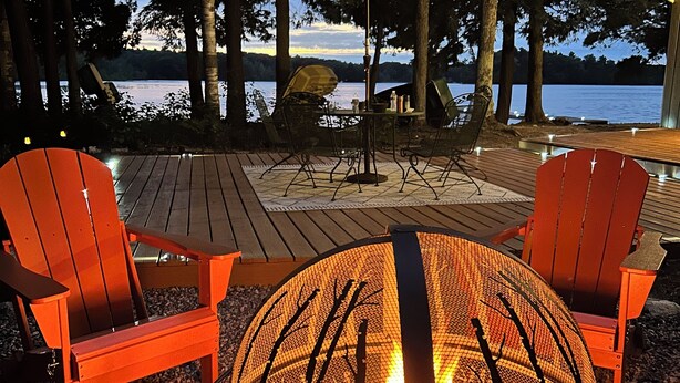 Une terrasse dotée d’un foyer extérieur, de sièges et offrant une vue sur un lac au crépuscule.