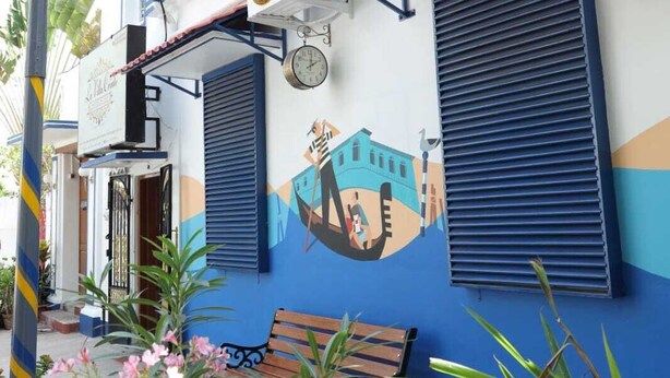 Un edificio con un mural que muestra una góndola, edificios, un reloj y un banco al frente.