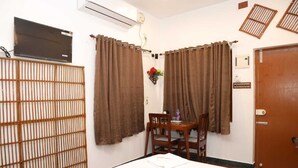 Una habitación con cama, una mesa y sillas, un televisor en la pared y una puerta.