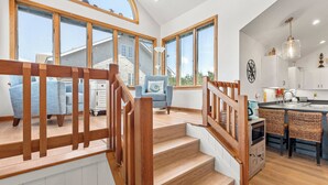 A modern kitchen with a central island, large windows, and a staircase with wooden railings. - 6BR Duck Resort | Hot Tub, Beach & Village Walk (Duck)