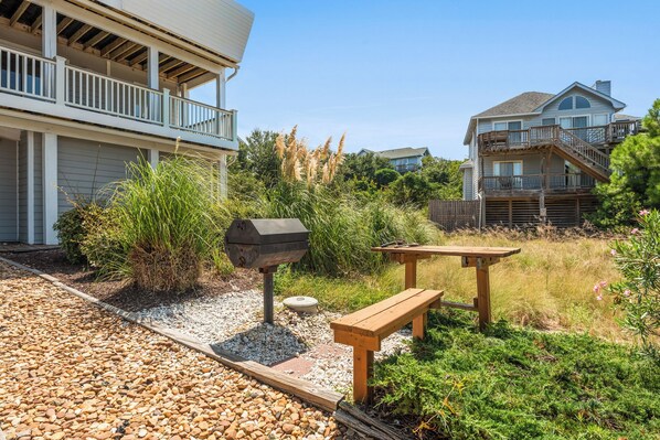 A backyard with a barbecue grill, wooden picnic table, and a small garden area with gravel and plants.